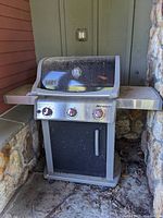 Full view of the Weber Spirit gas grill showing the black main body, stainless steel control panel, side shelf, and lid with built-in thermometer.