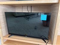 Front view of the 32 inch Samsung TV on wooden shelving, screen off with visible stand legs and no remote visible.