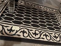 Close-up photo of one black and white area rug showing the geometric pattern and decorative border, placed on a basement floor.