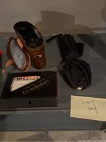 Set including binoculars with leather case, boxed dominoes set, and folded black umbrella on display surface.