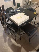Card table with 4 black folding chairs and 2 brown wooden folding chairs in basement, table stacked with miscellaneous items not included.