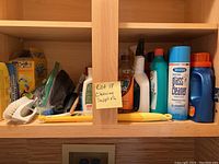 Shelf with various cleaning supplies, detergents, sponges, brushes, and bottles including a bottle of Sprayway glass cleaner.