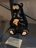 Front view of a glossy black ceramic cookie jar shaped like a bear holding a cookie with a label 'Lot 42 cookie jar' next to it.