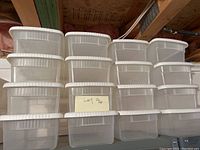 16 empty translucent plastic shoe boxes stacked in four rows with white lids on top, photo taken in basement showing the condition as needing cleaning.