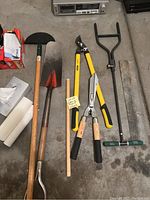 Photo showing shovels, garden pick, sheets, lopper pruners, and yard butler laid out on floor