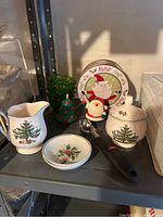 Overview of all items on metal shelf showing sugar and creamer set, Santa plate and figurine, small green tin, and small Christmas tree.