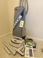 Full view of upright Oreck XL vacuum with cloth bag and base, showing included attachments and bags around it