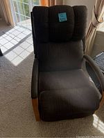 Front view of small dark gray fabric upholstered rocker recliner chair with cushioned back and wooden armrests. Chair has a note indicating footrest issue.