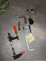 Various metal clamps on concrete floor showing different types and handles