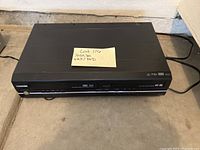 Toshiba VHS/DVD player front view showing VHS slot, DVD tray, and control buttons.