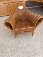 Front view of the brown wicker armchair showing the curved arms and high backrest.