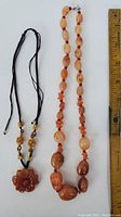 Full view of both agate necklaces with ruler for scale, showing the carved flower pendant and the large polished beads.