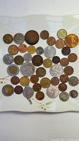 Top-down view of the assortment showing about 40 assorted coins of differing sizes and tones spread on a flat white surface.