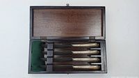 Set of four silver plate butter knives in wooden box with green felt lining.