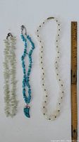 Photo of three gemstone necklaces showing overall length with ruler for scale. Includes pale green chip necklace, turquoise chip necklace with turquoise pendant, and white bead necklace with spacers.