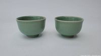 Front view of two green glazed ceramic teacups side by side showing exterior and interior surfaces