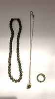 Full view of all three pieces: a green jade bead necklace, a gold-tone chain with dolphin pendant, and a jade ring.