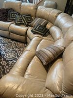Beige leather sectional sofa curved with throw pillows on top, resting on patterned area rug.