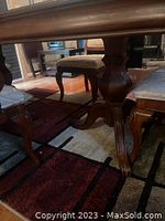 Close-up side view of wood dining table base and cushioned wooden dining chairs on carpeted floor