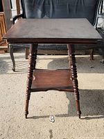 Front view of the antique Victorian square table with solid mahogany turned legs and bottom shelf.