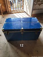 Closed vintage French blue trunk with brass fittings placed on a wooden floor, showing exterior details and color.
