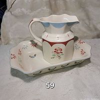 Photo of the ceramic pitcher placed on the matching tray, showing the floral and bird pattern decoration with a scalloped edge on the tray and scalloped rim on the pitcher.