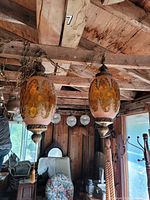 Two vintage amber glass hanging lamps suspended from wooden ceiling beams in a rustic room. Both lamps have textured amber glass with ornate metal detailing and hanging chains.