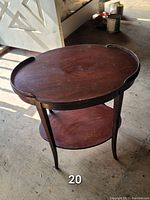 Full view of the 2 tier mahogany side table, showing oval top with scalloped edges and lower oval shelf with four curved legs.