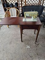 Full view of sewing machine in wooden cabinet with fold-out wing extension, placed in outdoor setting.