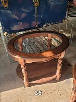 Full view of the vintage round side table with glass top, wooden frame and lower shelf, showing the turned wood legs and the clear glass center.
