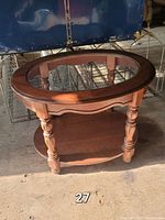 Photo showing the vintage side table with round glass inset top, turned legs, and wooden lower shelf in a warehouse setting.