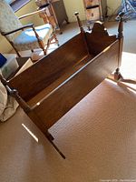 View of the cradle showing its rectangular form, side panels, and turned posts with finials.