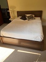 Full view of bed with headboard and footboard, made of wood with a brown finish, mattress and pillows included for size reference