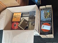 Two cardboard boxes filled with various music CDs, edges worn, assorted album covers visible including Cash album and others