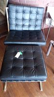 Full view of black leather tufted chair and matching ottoman on metal frames
