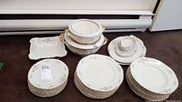 Photo showing stacks of plates arranged by type and two white serving bowls with gold handles at the back