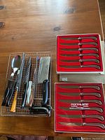 Overview showing two boxed steak knife sets and various loose serving and carving utensils on a wooden table.