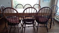 Set of eight wooden dining chairs around a wooden dining table viewed from behind.