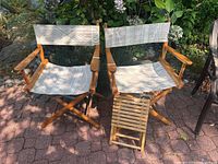 Front view of both director chairs and the small slatted wood side table positioned between them outdoors on a brick patio.