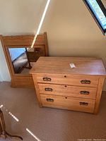 Front angle view of dresser with three drawers and matching wood framed mirror resting against wall.
