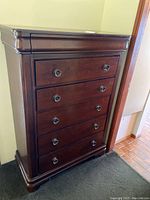 Front view of the wood dresser showing five visible drawers with round metal knobs and the curved top edge.