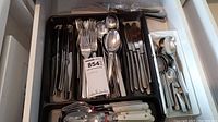 Drawer organizer with mixed flatware including forks, spoons, knives, and serving spoons arranged inside.