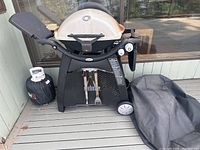 Weber propane grill with silver rusted lid, side burner with cover, propane tank and two grilling tools hanging below.