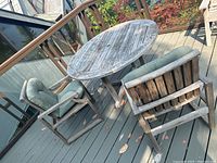 Photo showing two teak outdoor chairs with green cushions around a round teak table on deck, highlighting overall set condition and weathering