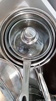 Top view of stacked stainless steel cooking pots, some with glass lids that have stainless steel knob handles.