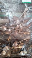 Multiple small sugar spoons and dessert forks in resealable plastic bags on dark surface
