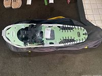 Top view of one Orvis snowshoe showing aluminum frame, green decking, and black binding on black carrying bag.
