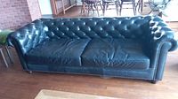 Full front view of black leather sofa showing button-tufted back, two seat cushions and rolled arms with brass nailhead trim