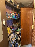 Photo of narrow storage shelves holding assorted spray cans, tools, small containers, and other hardware items.