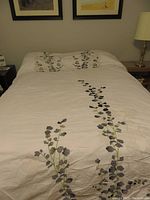 Bed made with white duvet cover decorated with embroidered gray and black leaves and branches.
